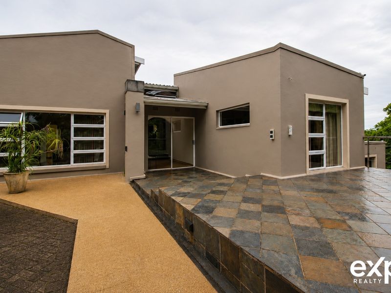 A modern rear exterior view featuring a spacious tiled patio, sliding glass doors, and clean architectural lines with paved pathways.