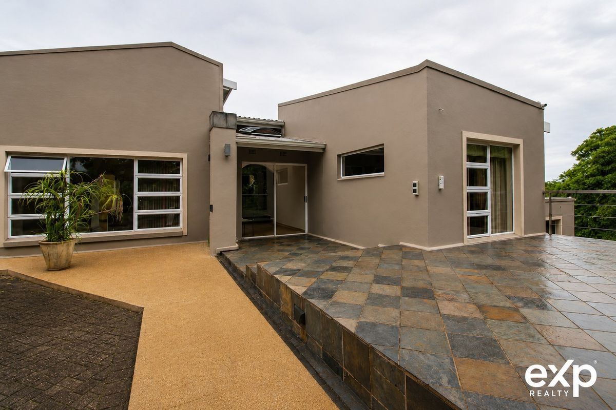 A modern rear exterior view featuring a spacious tiled patio, sliding glass doors, and clean architectural lines with paved pathways.