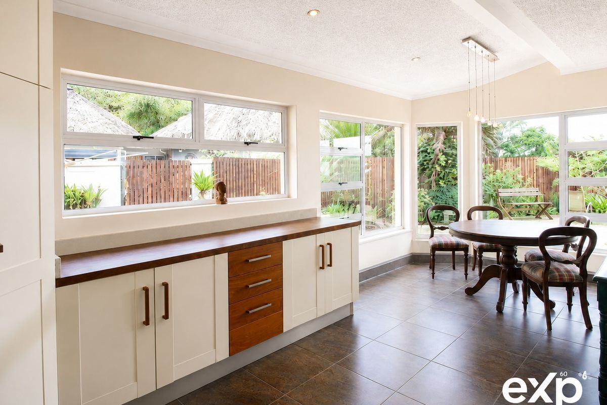 A bright, modern kitchen featuring custom cabinetry with timber countertops, tiled flooring, and large windows overlooking the garden.