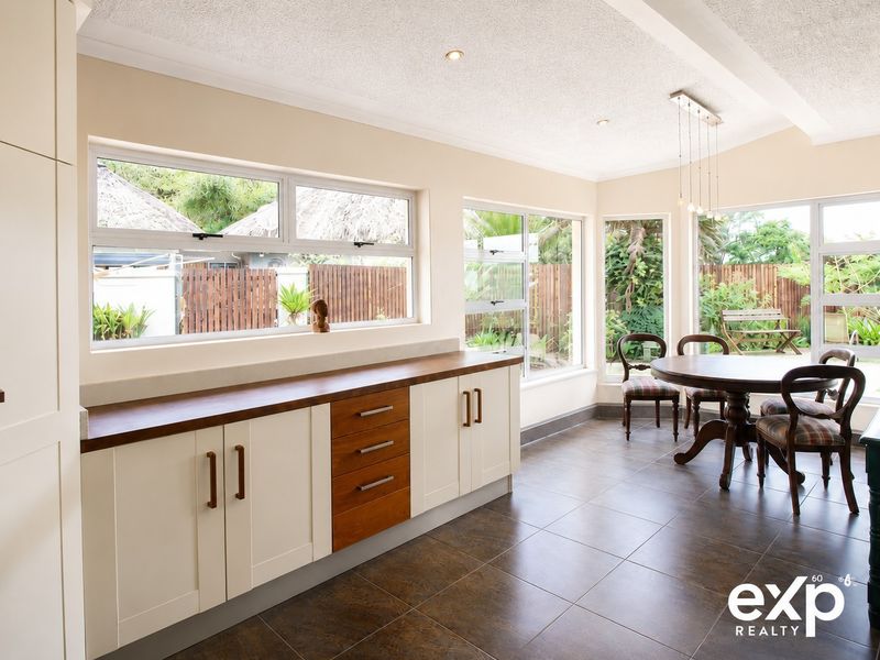 A bright, modern kitchen featuring custom cabinetry with timber countertops, tiled flooring, and large windows overlooking the garden.