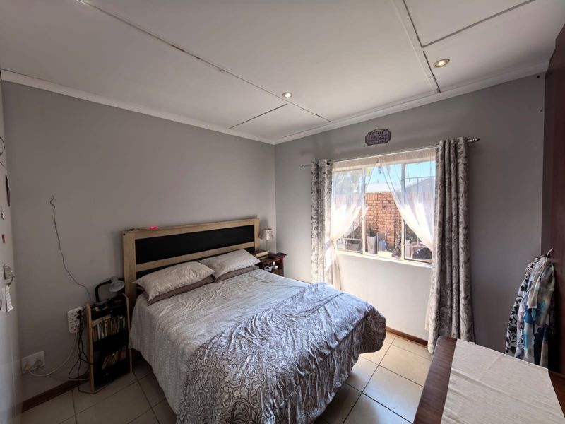 A functional bedroom featuring tiled flooring, recessed ceiling lighting, and a window fitted with security bars, providing natural light and ventilation.