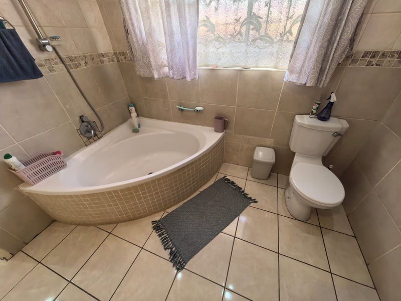 A functional bathroom featuring a corner bathtub with tiled surround, ceramic wall and floor tiling, and a standard toilet.