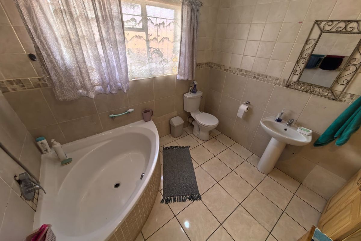 A functional bathroom featuring a corner bathtub, pedestal sink, and toilet, finished with neutral ceramic wall and floor tiling.