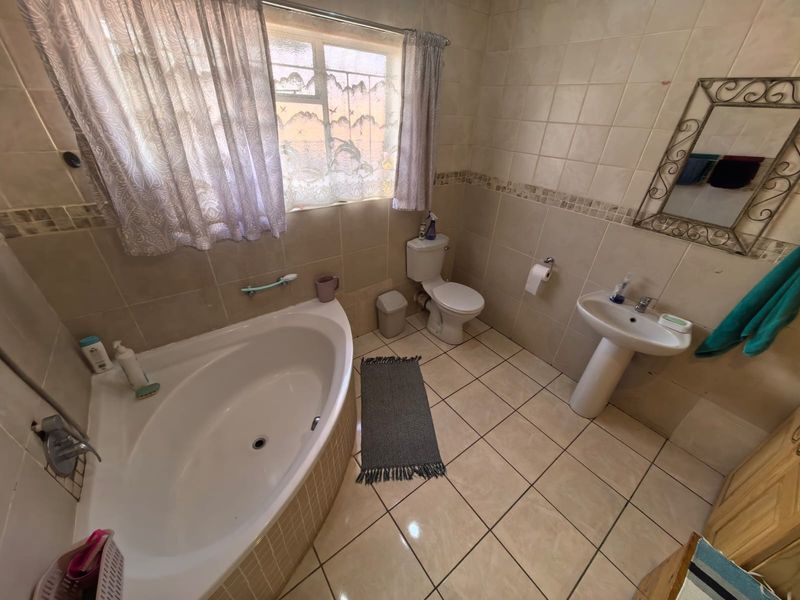 A functional bathroom featuring a corner bathtub, pedestal sink, and toilet, finished with neutral ceramic wall and floor tiling.