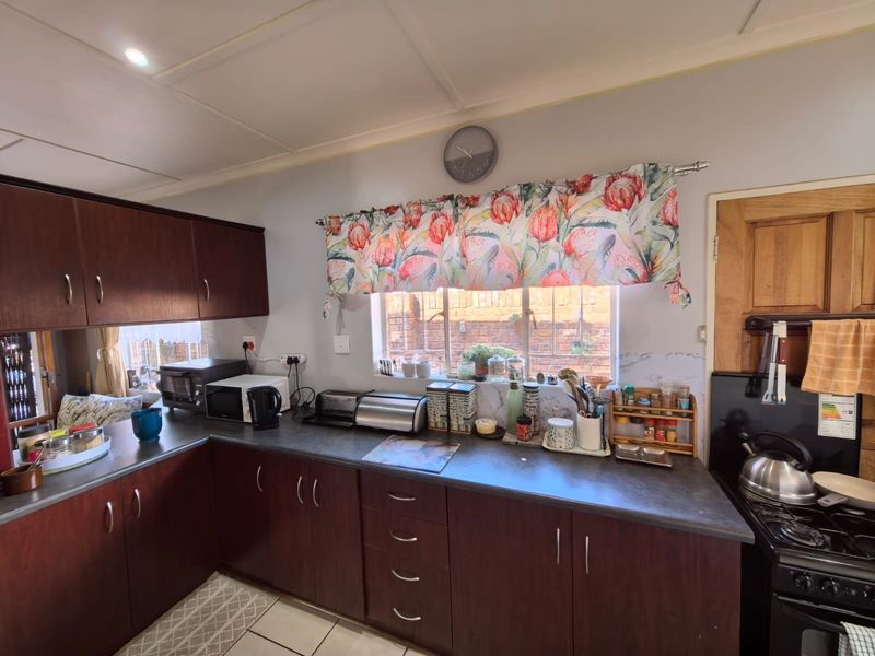 A functional kitchen featuring dark wood cabinetry, laminate countertops, tiled flooring, and a built-in stove, offering a practical layout for daily meal preparation.
