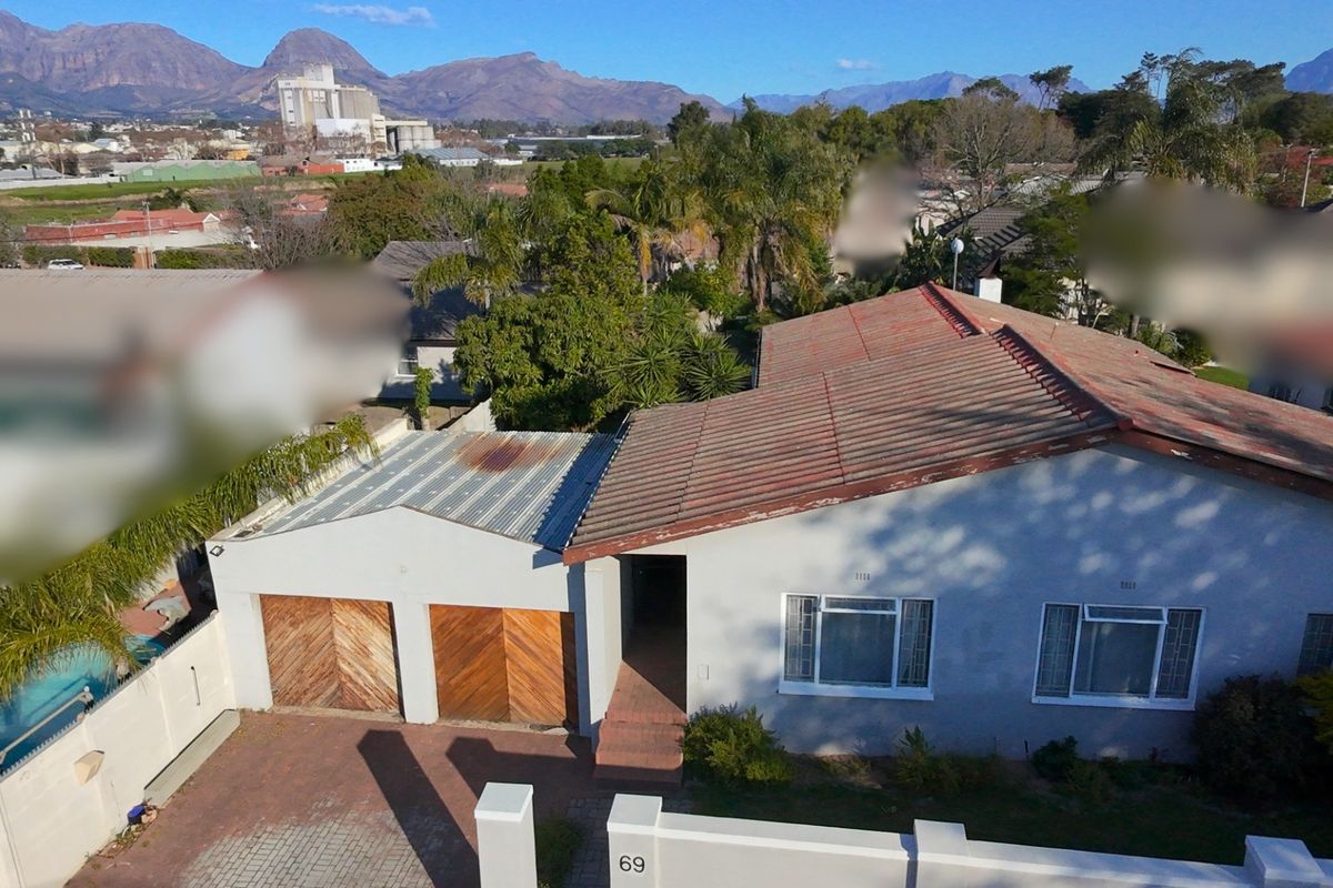 Aerial view of a residential property featuring a double garage, paved driveway, and a combination of tiled and corrugated metal roofing.