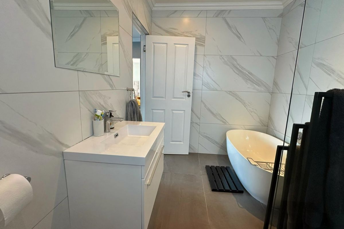 Modern bathroom featuring a sleek freestanding bathtub, contemporary vanity with integrated sink, and elegant marble-look wall tiling.
