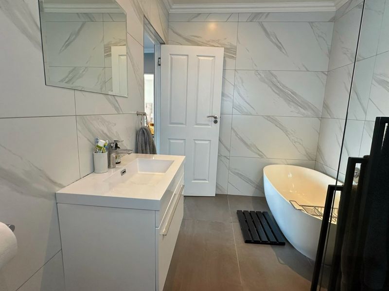 Modern bathroom featuring a sleek freestanding bathtub, contemporary vanity with integrated sink, and elegant marble-look wall tiling.
