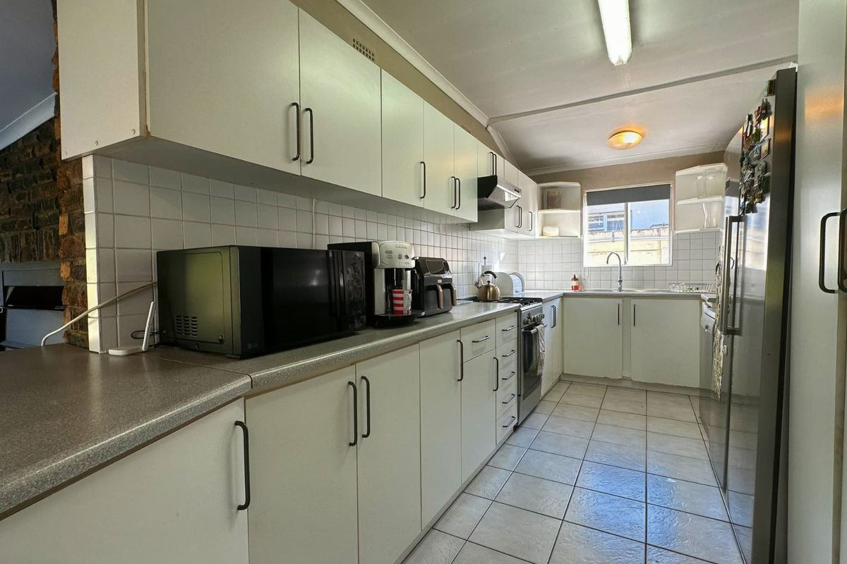 A functional galley-style kitchen featuring white cabinetry, laminate countertops, tiled backsplash, and ceramic flooring, offering a practical layout for daily meal preparation.