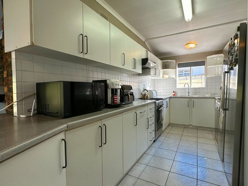 A functional galley-style kitchen featuring white cabinetry, laminate countertops, tiled backsplash, and ceramic flooring, offering a practical layout for daily meal preparation.