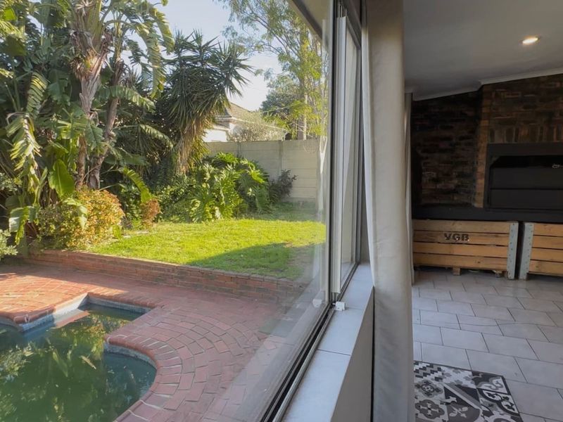 Covered patio area featuring a built-in brick braai, tiled flooring, and direct access to a swimming pool and garden.