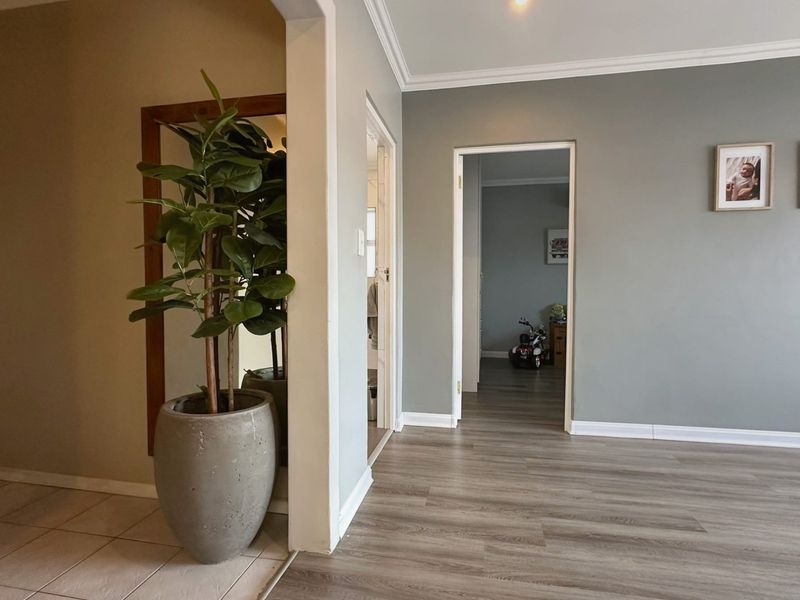A bright, neutral hallway featuring a transition between tiled and laminate flooring, accented by crown molding and a classic architectural archway.