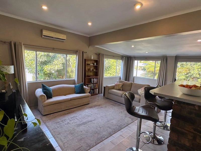 Spacious open-plan living area featuring tiled flooring, recessed downlighting, a split-system air conditioner, and a brick breakfast bar overlooking the lounge space.