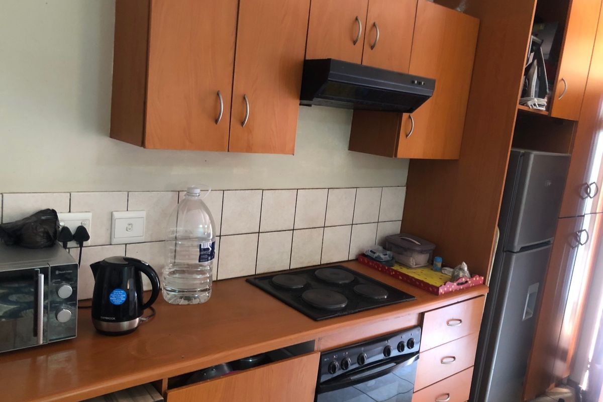 A functional kitchen featuring wood-look laminate cabinetry, a built-in electric oven and hob, and a tiled splashback, offering a practical layout for daily use.