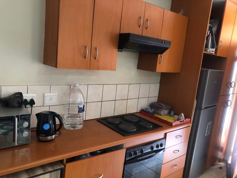 A functional kitchen featuring wood-look laminate cabinetry, a built-in electric oven and hob, and a tiled splashback, offering a practical layout for daily use.