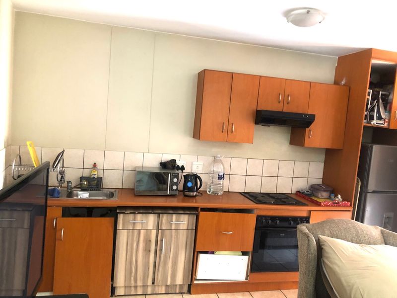 A dated kitchen featuring wood-tone cabinetry, laminate countertops, a built-in oven, and an electric hob, requiring cosmetic updates to improve functionality and aesthetic appeal.