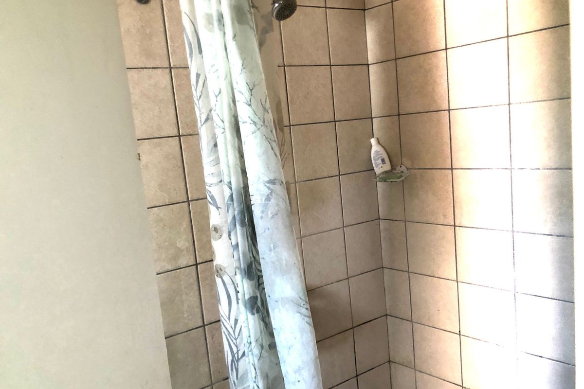 A shower enclosure featuring tiled walls and a standard shower head, showing signs of wear and discolored grout.