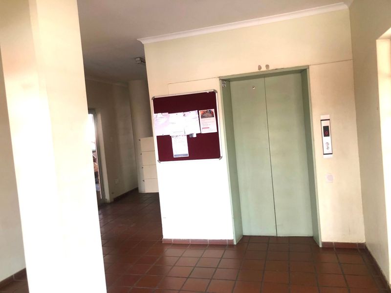 A communal apartment building hallway featuring a functional elevator, tiled flooring, and neutral wall finishes.