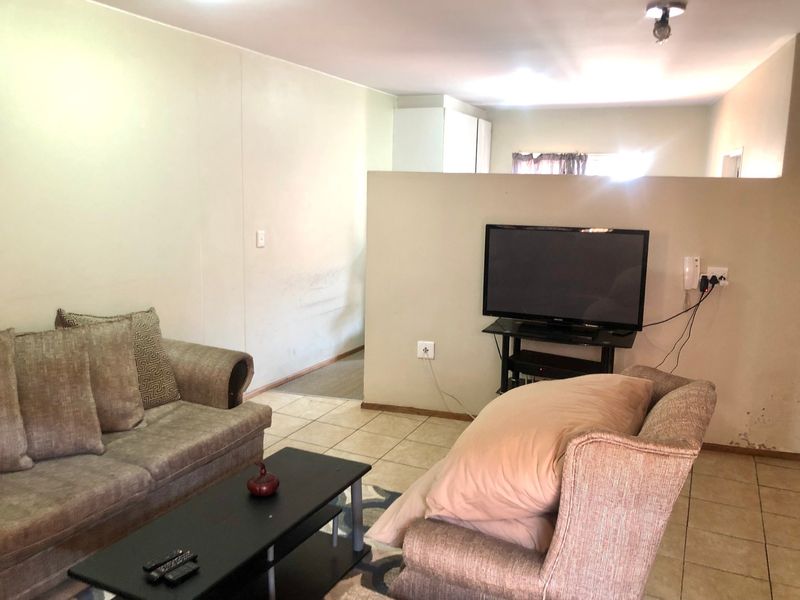 A living area featuring tiled flooring and a partial room divider, providing a functional layout with visible wall wear requiring maintenance.