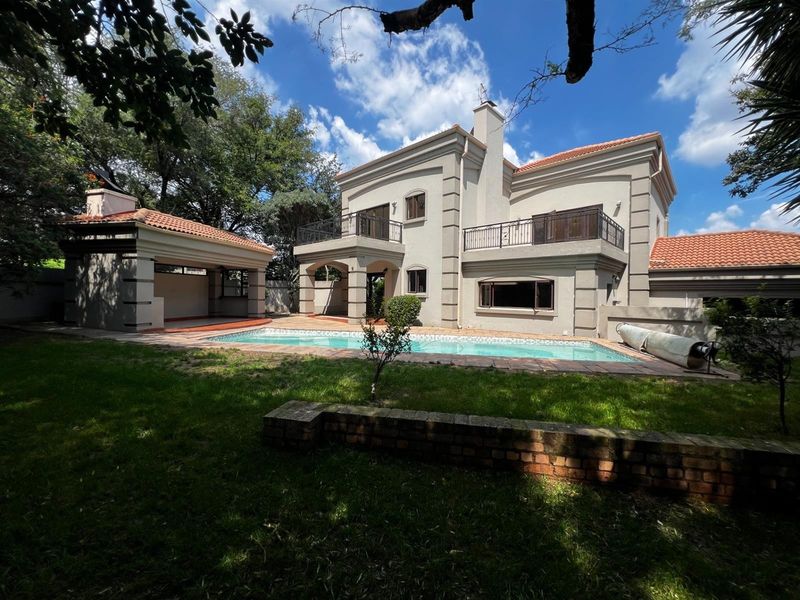 Rear view of a two-story house featuring a swimming pool, covered patio area, and upper-level balconies set within a landscaped garden.