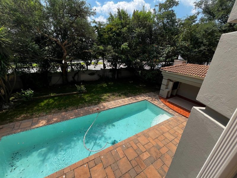 An elevated view of a backyard featuring a swimming pool with a tiled deck and a covered patio area with a built-in braai.
