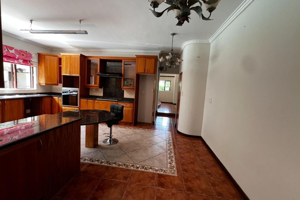 Spacious kitchen featuring wooden cabinetry, granite countertops, built-in oven, extractor fan, and a breakfast bar, with tiled flooring throughout.