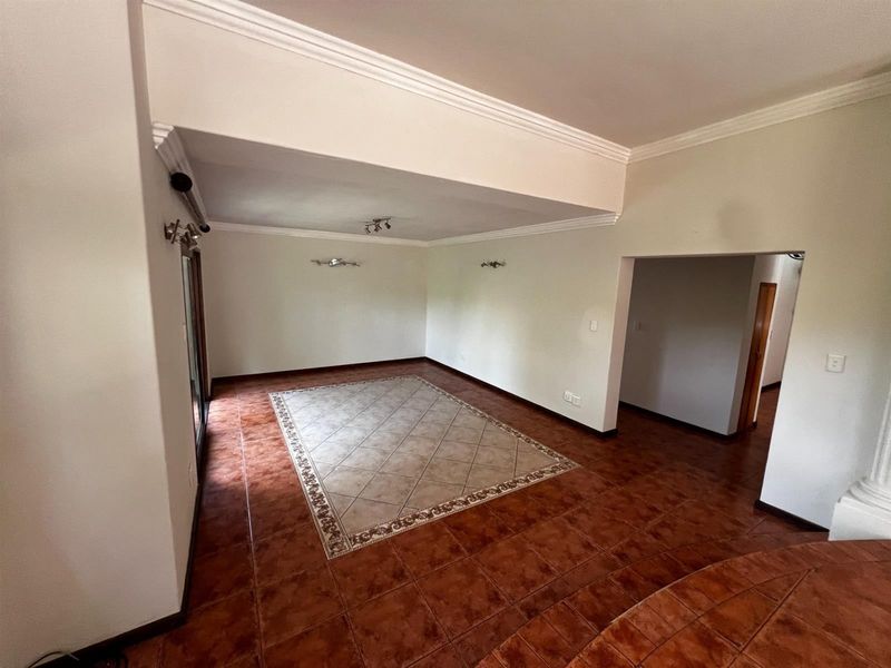A spacious, empty living area featuring ceramic tile flooring, decorative crown molding, and wall-mounted lighting fixtures, offering a versatile blank canvas.