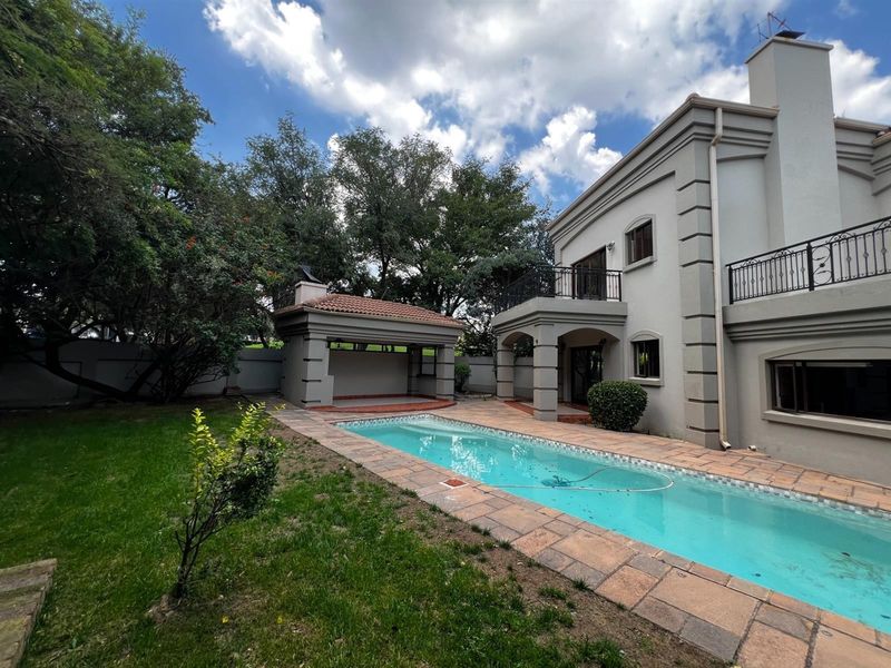 Rear exterior view featuring a swimming pool, paved surround, covered patio area, and a two-story house facade with a balcony.