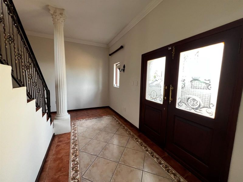 Spacious entrance hall featuring decorative column, wrought iron staircase railing, and elegant tiled flooring with a detailed border.
