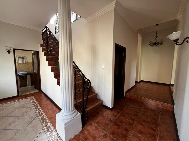 Spacious entrance hall featuring a tiled staircase with wrought iron balustrades, decorative column, and ceramic flooring leading to adjacent living areas.