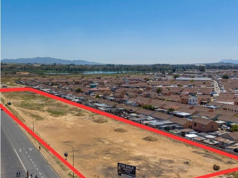 Aerial view of a vacant commercial industrial plot located along a main road, highlighting the property boundaries and surrounding residential area.