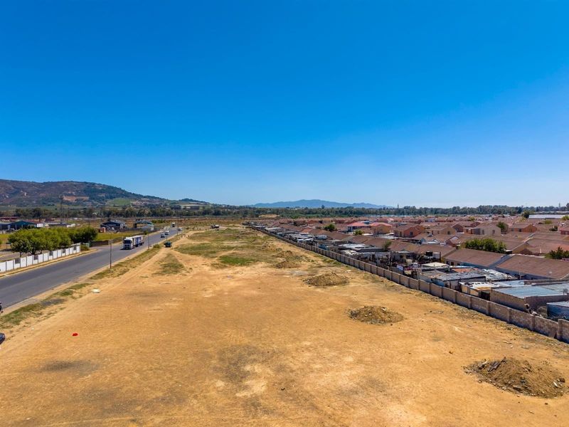 Aerial view of a large, undeveloped commercial land parcel adjacent to a public road and residential area.