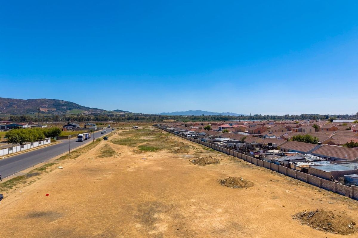 Aerial view of a large, undeveloped commercial land parcel adjacent to a public road and residential area.