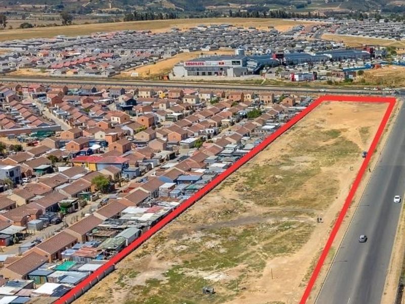 Aerial view of a large, vacant commercial development plot situated in a high-visibility location adjacent to a main road and residential area.