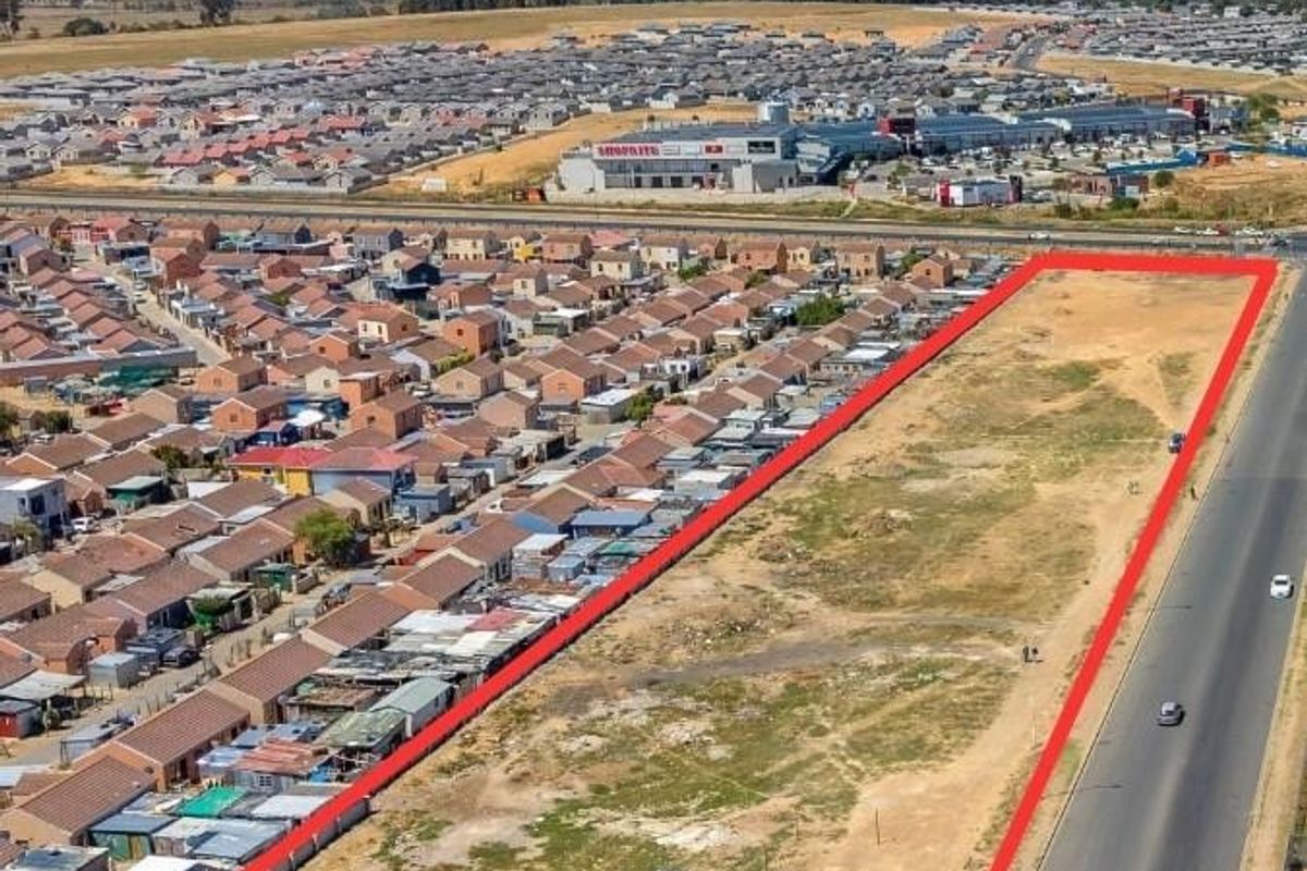 Aerial view of a large, vacant commercial development plot situated in a high-visibility location adjacent to a main road and residential area.