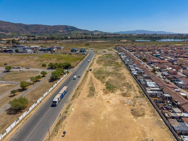 Aerial view of a commercial property site adjacent to a main road, featuring open land and surrounding residential infrastructure.