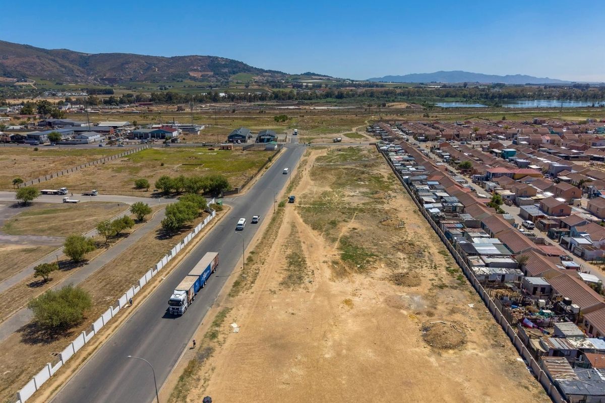 Aerial view of a commercial property site adjacent to a main road, featuring open land and surrounding residential infrastructure.