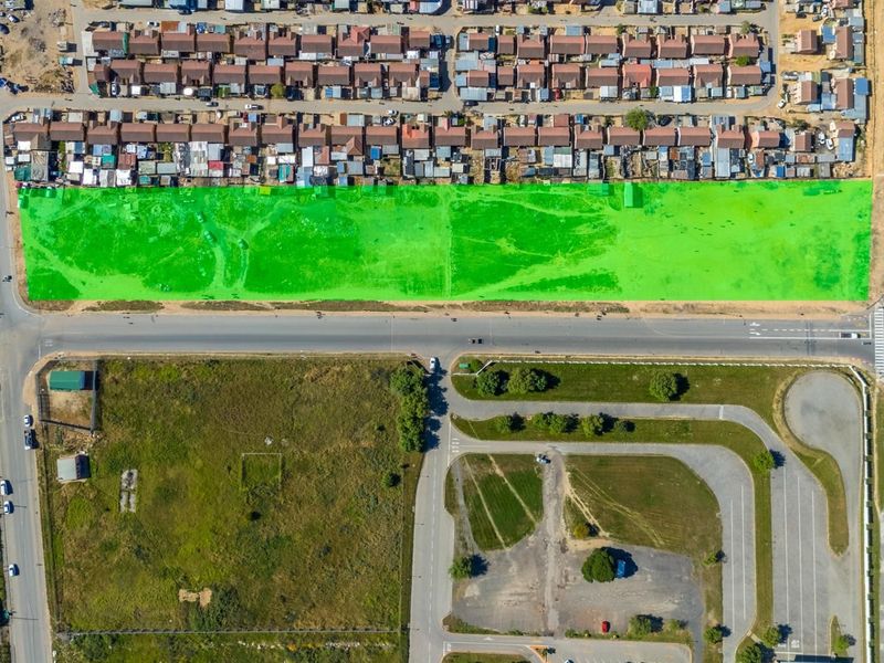 Aerial view of a commercial property site featuring undeveloped land, adjacent paved parking, and surrounding residential infrastructure.