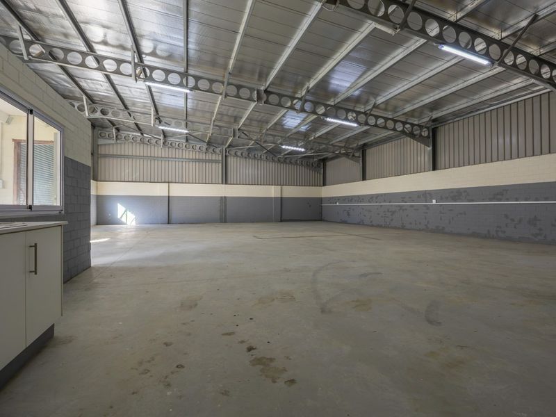 Spacious industrial utility area featuring exposed steel trusses, concrete flooring, and painted blockwork walls, suitable for storage or workshop use.
