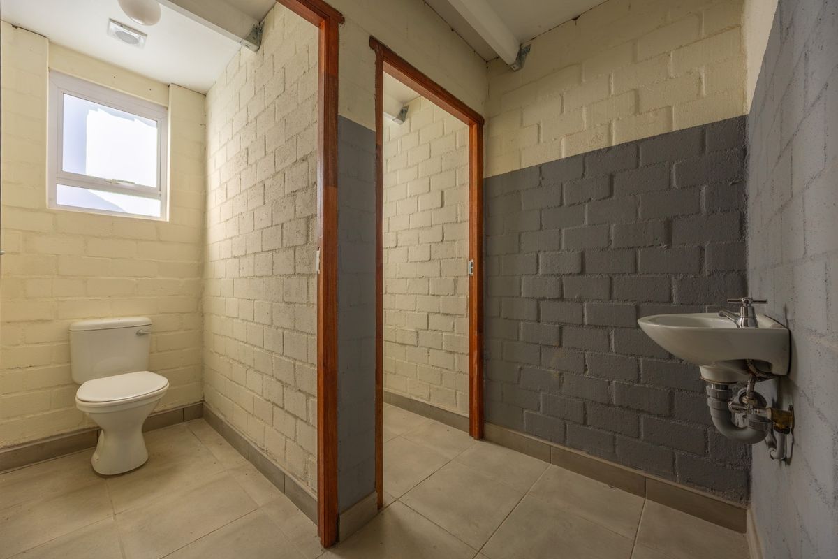 A functional industrial-style bathroom featuring exposed brick walls, tiled flooring, a wall-mounted basin, and a separate toilet cubicle.