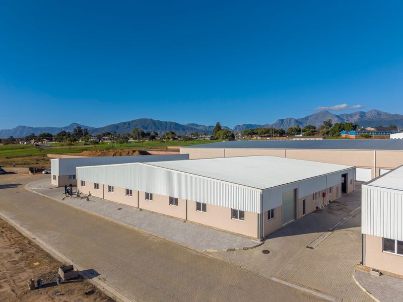 Aerial view of a modern industrial warehouse complex featuring corrugated metal roofing, brick exterior walls, and paved access areas.