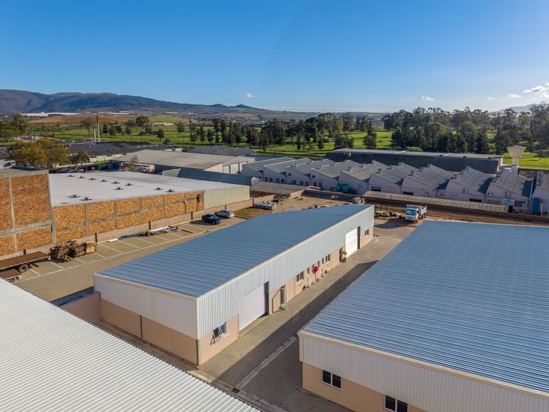 Aerial view of an industrial complex featuring multiple warehouse units with metal roofing, roller shutter doors, and paved access areas.