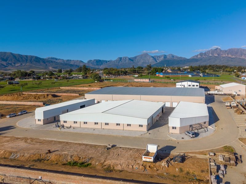 Aerial view of an industrial property complex featuring multiple warehouse buildings with metal roofing and paved access areas set against a mountain backdrop.