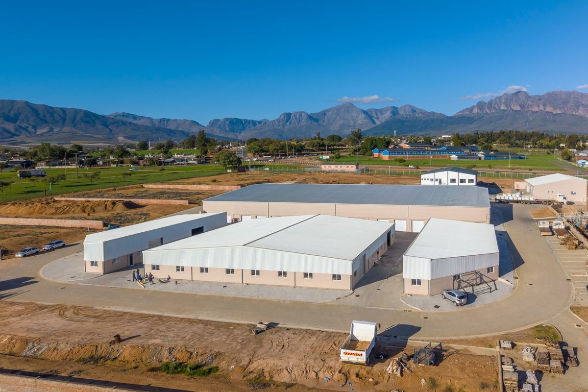 Aerial view of an industrial property complex featuring multiple warehouse buildings with metal roofing and paved access areas set against a mountain backdrop.