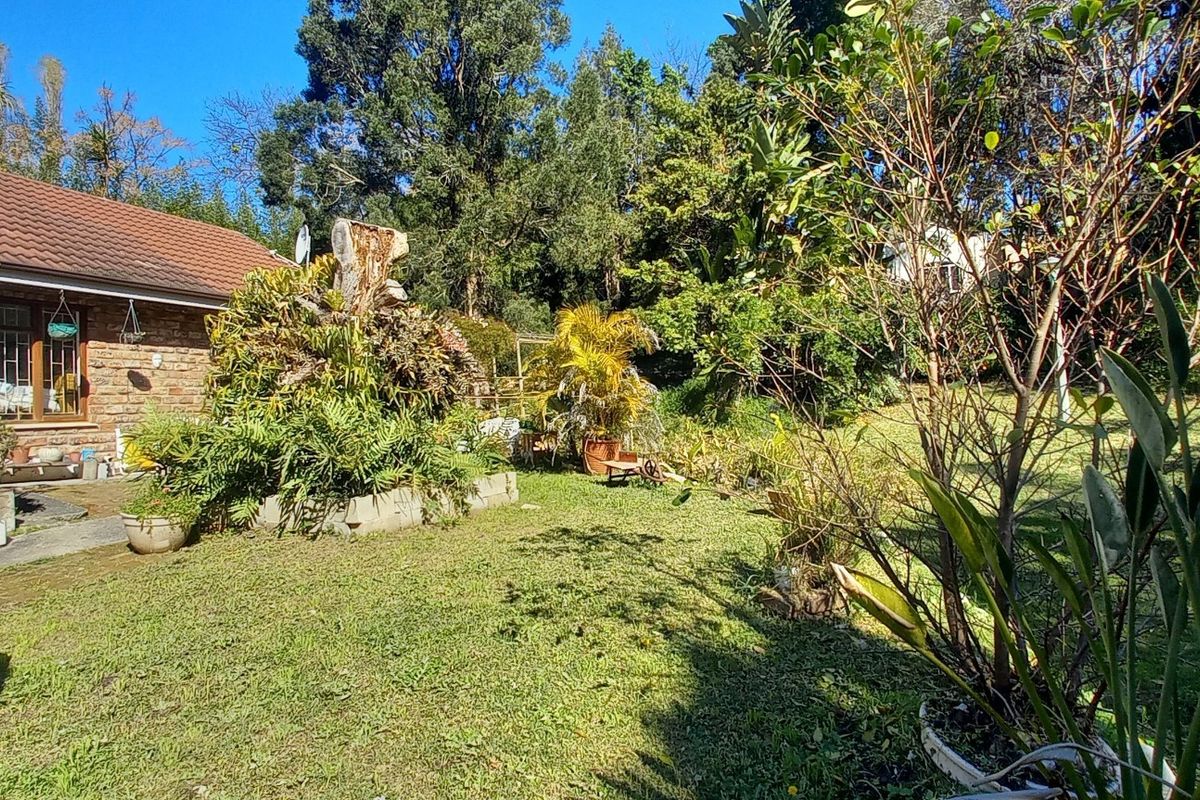 A view of the rear garden and brick-clad house exterior featuring a tiled roof, chimney, and paved patio area.