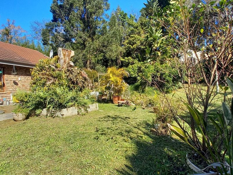 A view of the rear garden and brick-clad house exterior featuring a tiled roof, chimney, and paved patio area.