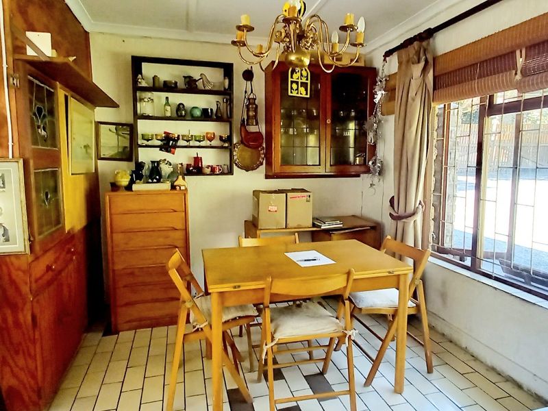 A dining area featuring built-in wooden cabinetry, tiled flooring, and a large window with security bars, offering a dated but functional space.