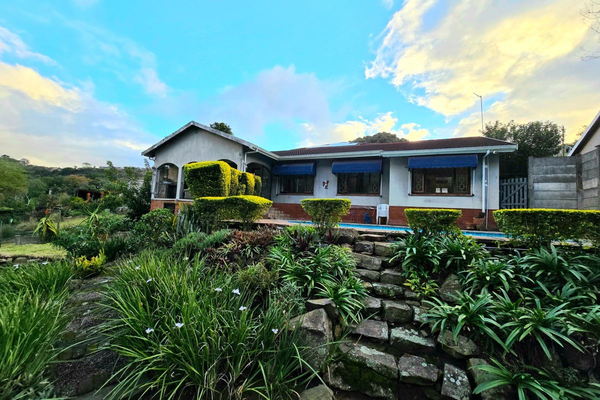 Rear view of the house featuring a swimming pool, established garden, stone landscaping, and covered patio area.