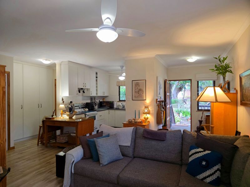 An open-plan living and kitchen area featuring laminate flooring, ceiling fans, and functional built-in cabinetry with direct access to the rear garden.