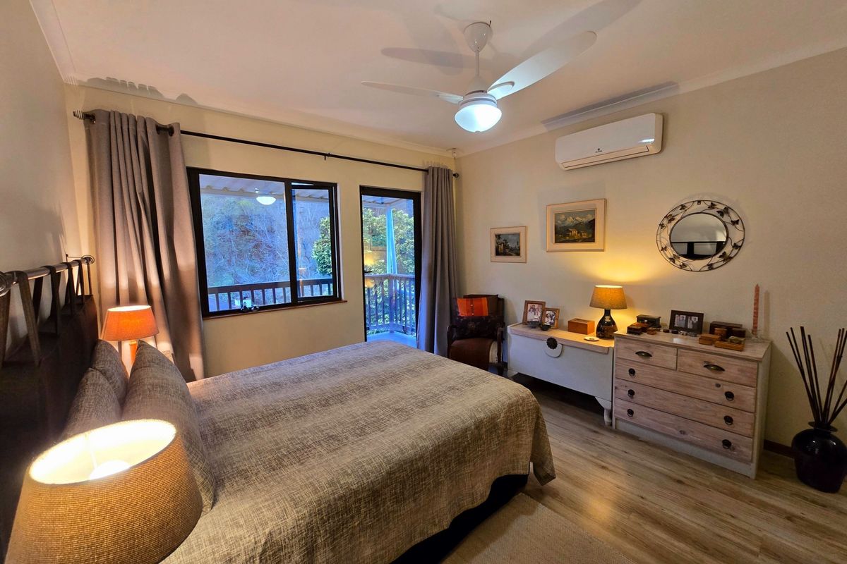A well-maintained bedroom featuring laminate flooring, a ceiling fan, and a split-system air conditioner, with direct access to an outdoor balcony.